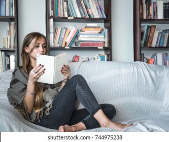 the girl with long hair dressed comfortably reading a book on the couch in the background of the library, the concept of reading and leisure time weekends - Shutterstock ID 744975238