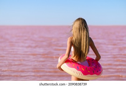 A Girl With Long Hair And A Pink Rubber Ring Looks At A Pink Lake In Summer.