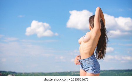 Girl long hair posing sexy naked erotic breasts. Woman sexy sticker nipples sun tanning. Female unrecognizable face posing denim shorts and naked sexy breasts sky background. Sexy lady concept.