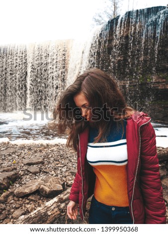 Girl with long hair standing and looking at the Waterfall on a gloomy cloudy day, Estonia
