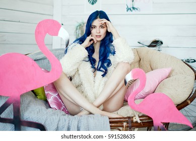 Girl With Long Legs And Blue Hair In A Fur Jacket Posing In A Chair With A Pink Flamingo In A Vintage Studio