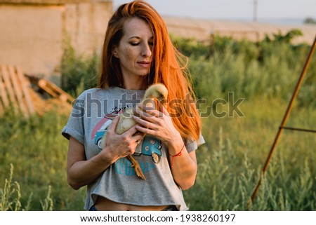 A girl with long red hair holds a young duck in her arms