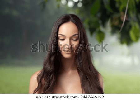 Girl with long wavy hair, downcast gaze and mysterious smile against backdrop of forest. Rest in nature, beauty and naturalness. Meditation and relaxation