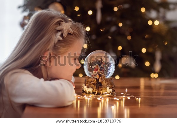 Girl looking at a glass ball with a scene of the birth of Jesus Christ in a glass ball on a Christmas tree