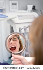 A Girl Looking At Her Reflection In A Hand Held Mirror.