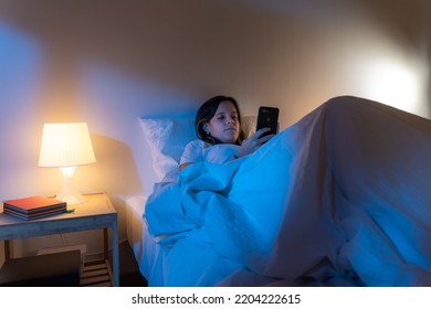 Girl Looking Her Smart Phone Doom Scrolling On Bed In The Middle Of The Night. Technology At Bed Concept.