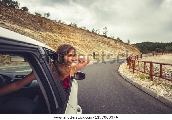 A girl is looking\
interested in the back seat in a car while someone is driving her\
in some rocky landscapes