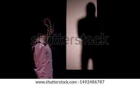 Girl looking at silhouette of criminal entering room, kidnapping concept, horror