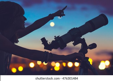 Girl looking at the stars with telescope beside her and de-focused city lights.