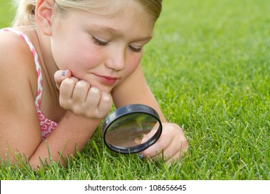 Girl Looking Through Magnifiying Glass At Grass Outdoors