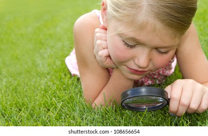 Girl Looking Through Magnifiying Glass At Grass Outdoors