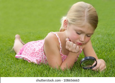 Girl Looking Through Magnifiying Glass At Grass Outdoors