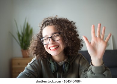 Girl Looks At Camera, Waves Her Hand And Smiles. Student Talks Over Internet. Video Conference Or E-learning At Home.