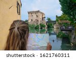 Girl looks at a map on the background of a historic bridge, Ponte Visconteo over the Mincio River, Italy