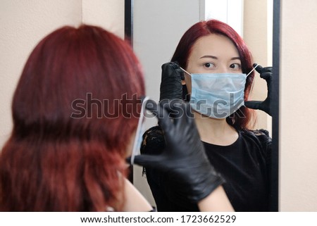 The girl looks in the mirror and puts on a blue protective mask