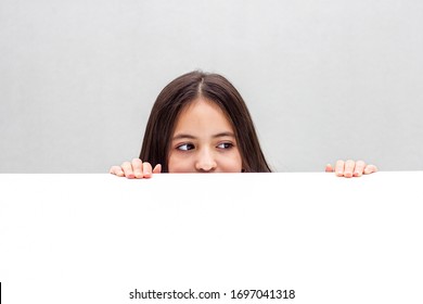 Girl looks out from behind the table. isolated on white background - Shutterstock ID 1697041318