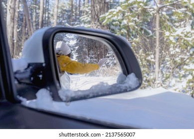 the girl looks out of the car window and waves her hand, the reflection in the side mirror of the car, the winter landscape around