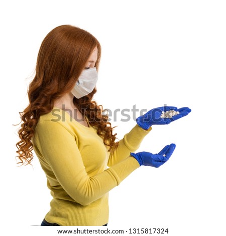 A girl with lush red hair in a gauze bandage and blue gloves holds a handful of pills on her palm. Side view. Personal protective equipment.