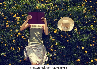 Girl lying in grass, reading a book. Intentionally toned. - Powered by Shutterstock