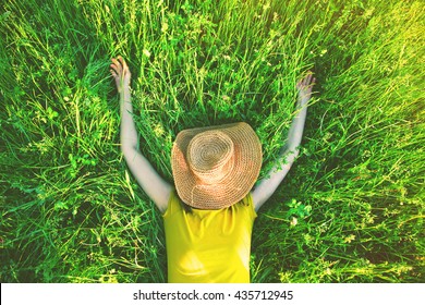 girl lying in grass with straw hat in summer sun