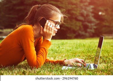 girl lying in the grass and using laptop and smart phone