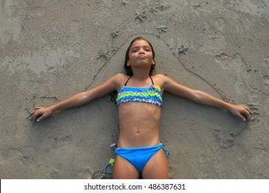 girl lying on beach with sea stars on her , young girl in bathing suit on the beach