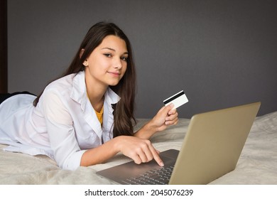 The Girl Is Lying On The Bed With A Laptop And Holding A Credit Card In Her Hand