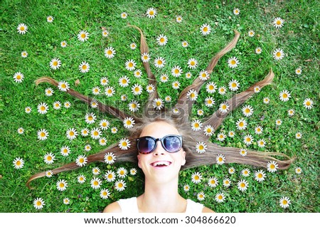 Girl lying on grass with her hair full of marguerites spread around her head