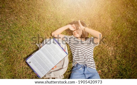 A girl lying on the meadow with a book and a bag on the side