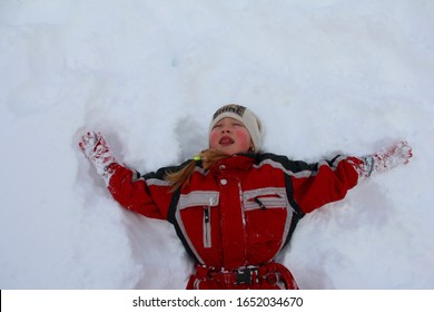 The Girl Is Lying On The Snow In A Red Ski Suit.