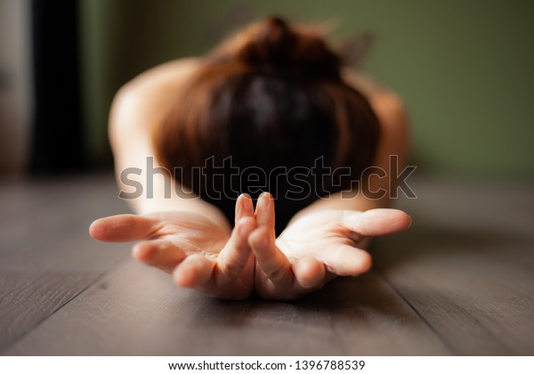 Girl lying in a relaxing yoga pose on a\
wooden floor, showing her hands, with her head lying on the floor\
and an unsharp background.