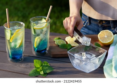 Girl makes summer refreshing cocktails blue lagoon. Close-up of adding ice cubes to glasses. Selective focus - Shutterstock ID 2122419455