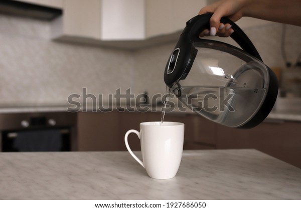 The girl makes tea
on the kitchen table. A woman pours boiling water into a white mug
on the kitchen table. The girl pours tea into a white mug from a
transparent teapot.