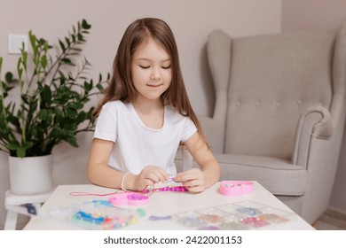Girl making pink and purple beaded jewelry at table in her room