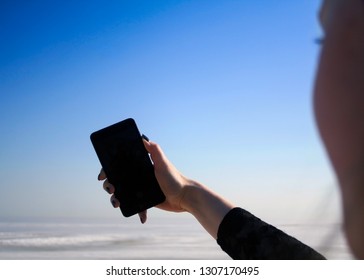 Girl Making Selfie On Front Camera Of Modern Smartphone, First Person View. Girl Holding Mobile Phone With Blank Mock Up Screen Area On The Sea Shore, Screen View