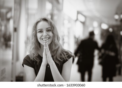 The girl in mall put hands in a prayer, looks on the camera smiles, asks a gift, monochrome