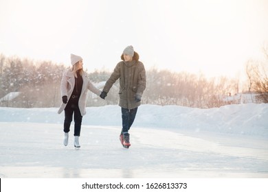 Girl and man are holding hands looking each other and eating on frozen ice of lake on skates. In background is sunset. - Powered by Shutterstock