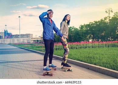 A girl and a man are riding in the park on a longboard