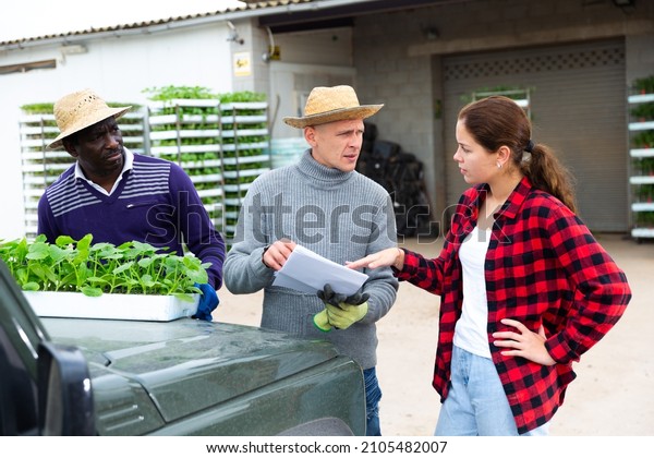 Girl manager discussing with men\
workers delivery of seedlings to the farm at a\
warehouse