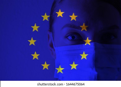 Girl In A Mask Against The Background Of The EU Flag. Fear Of Illness, Corona Virus 2019-2020. Virus, Outbreak And Mass Disease, Photo For News About The Corona Virus.