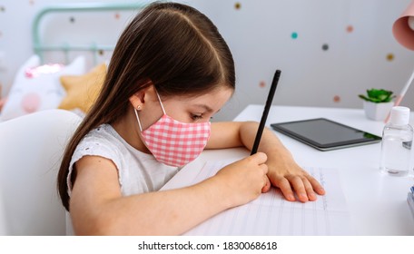 Girl with mask doing homework sitting at a desk in her bedroom