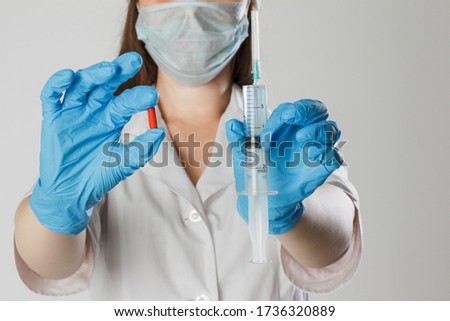 A girl in medical clothing and a mask holds a tablet and a syringe with a vaccine in blue latex gloves. Preparing for human vaccination shot and pills, medicine and drug concept.