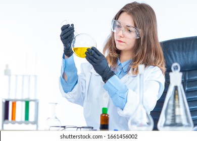 Girl In A Medical Laboratory. A Medical Worker Makes A Medicine. Pharmacologist In A Medical Laboratory. Young Formate In Safety Glasses. Lab Technician Holding A Large Flask In His Hands