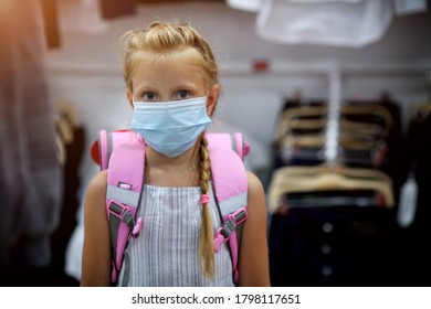 A Girl In A Medical Mask With A Briefcase On Her Back In A Shopping Center Is Going To School. Preparing For School After Quarantine Covid - 19. Protective Mask For The Prevention Of Coronavirus. 