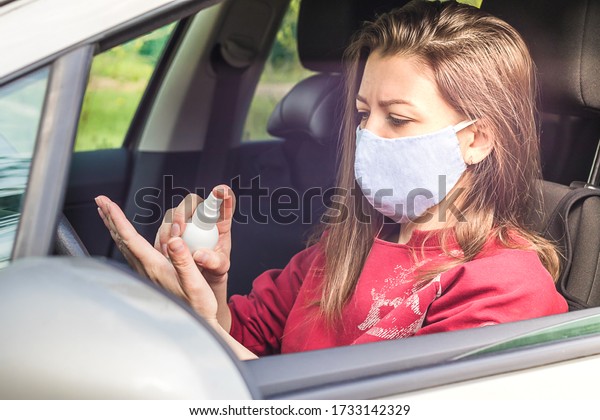 girl in medical mask in car\
treating her hands with disinfectant, sanitizer. woman using\
personal protective equipment to prevent coronavirus\
infection.