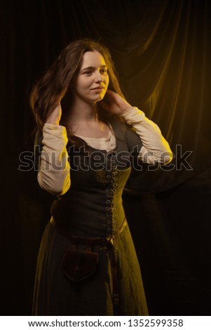 Girl in medieval dress and cloak in yellow light against a dark background
