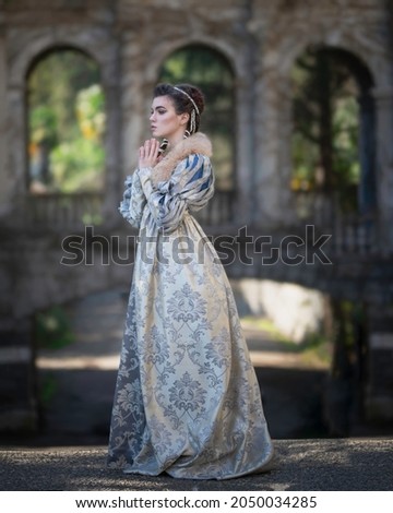 A girl in a medieval dress with prayerfully folded hands against the background of ancient arches