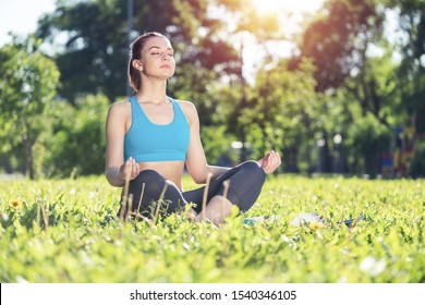 Girl meditates in lotus pose on green grass in park. Portrait of peaceful woman with closed eyes. Training and meditation outdoor at summer day. Harmony with nature and relaxation. Practicing of yoga.
