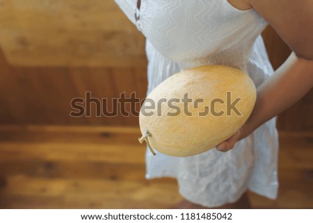 Girl with a melon in a rustic white dress on a wooden terrace