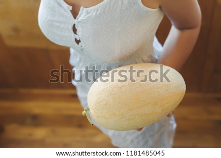 Girl with a melon in a rustic white dress on a wooden terrace
